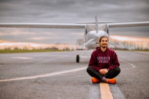 Male student sits in front of plane on runway
